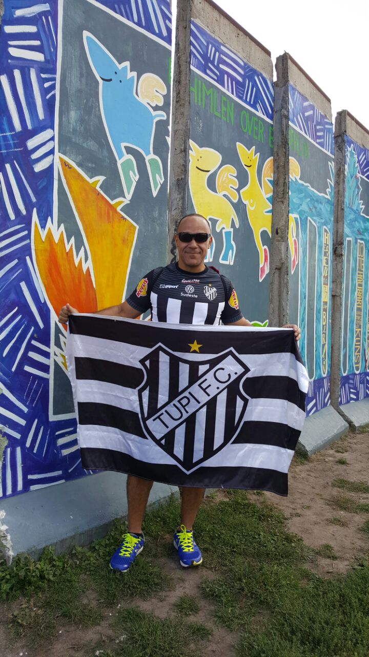 Sidney Barbosa está em Berlin para a maratona do próximo domingo e, ontem, exibiu a camisa e a bandeira do Tupi, ao lado do que sobrou do antigo “muro da vergonha”   