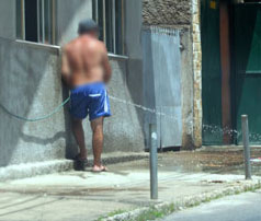 Homem usa mangueira para lavar calçada 