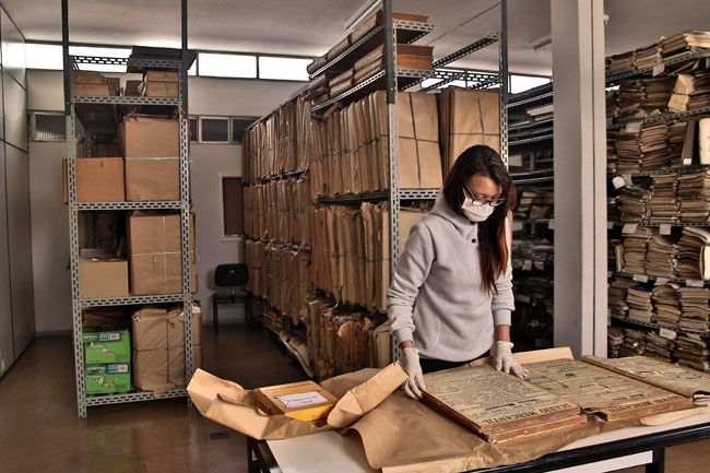 A estagiária Yasmin Corrêa manuseia um dos grossos volumes do acervo contendo mais de 70 anos de história da cidade (Fernando Priamo)