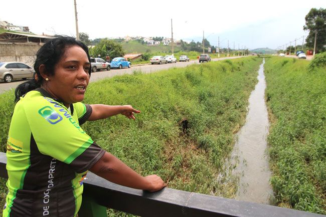 Elisângela mostra manilha que estaria fazendo água do córrego cair em ruas perpendiculares à via, atingindo moradias do entorno