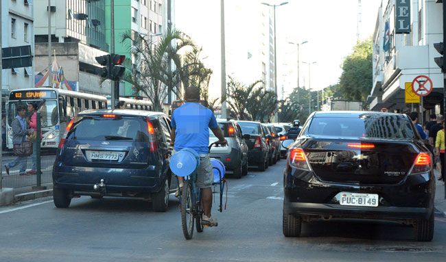 Apesar de sinalização indicar que ciclista deve circular à direita, homem se arrisca no meio de carros