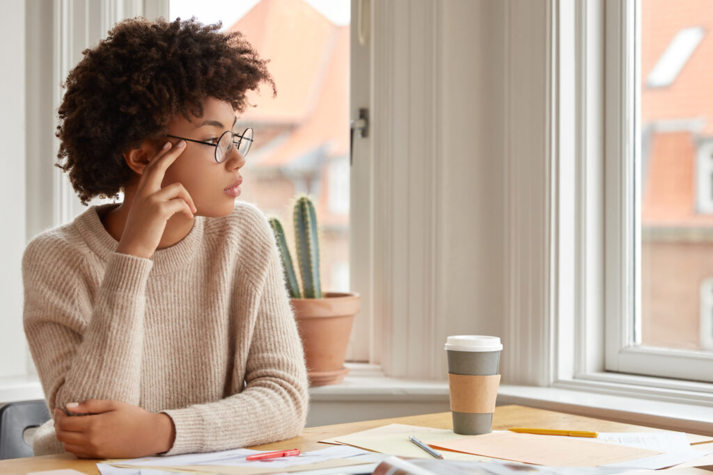 photo of contemplative woman with afro hairstyle wears round spectacles casual warm sweater