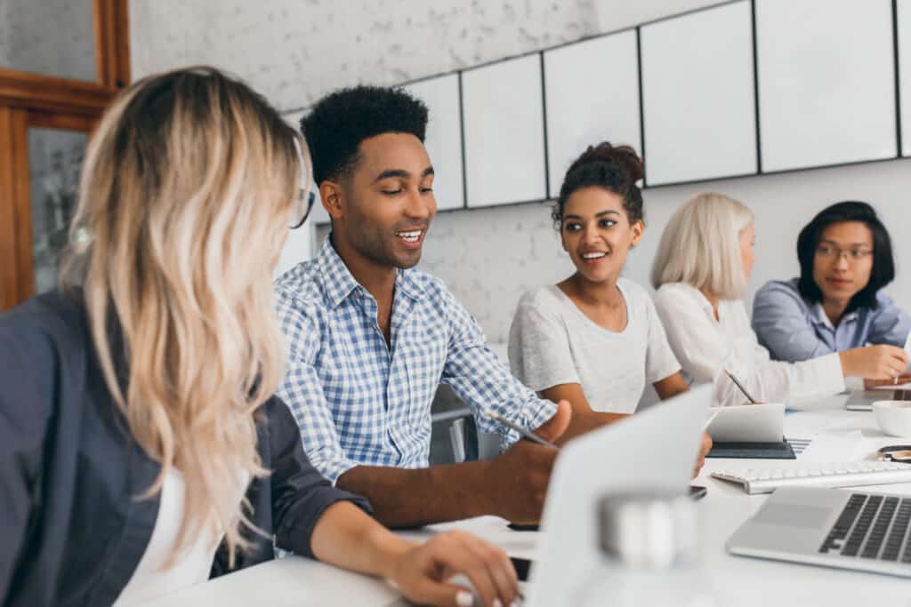 young woman with long blonde hair listening african man in blue shirt which using laptop indoor portrait of black and asian office workers talking during conference