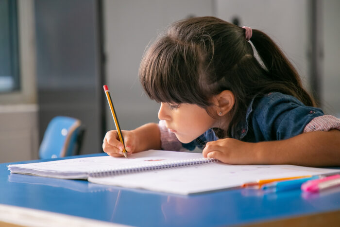 garota latina de cabelo concentrado sentada na mesa da escola e desenhando em seu caderno