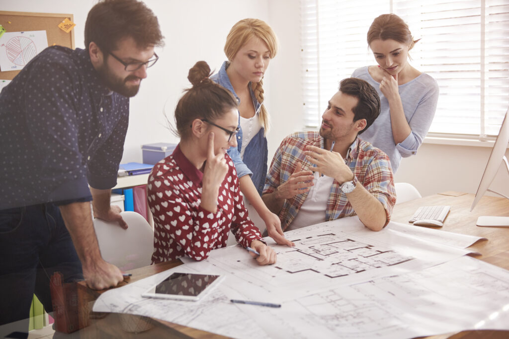 colegas de trabalho no escritorio com planos de arquitetura e um computador