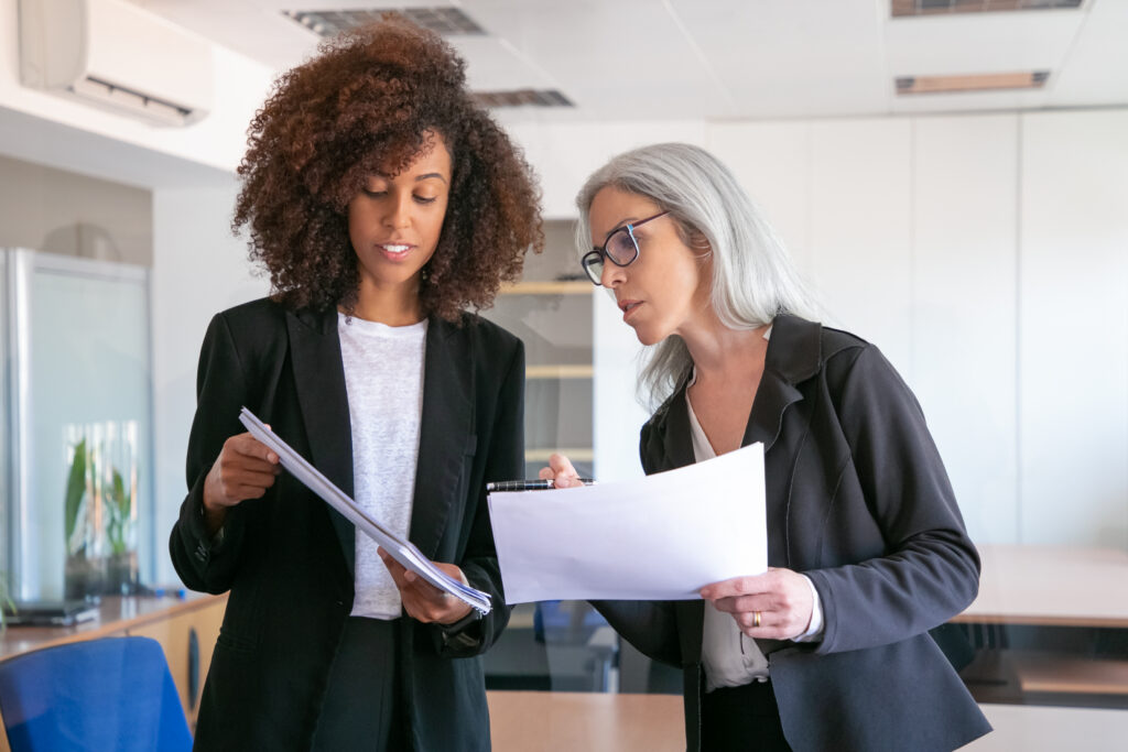 content young manager showing document adult colleague two pretty content female colleagues holding papers standing office room teamwork business management concept