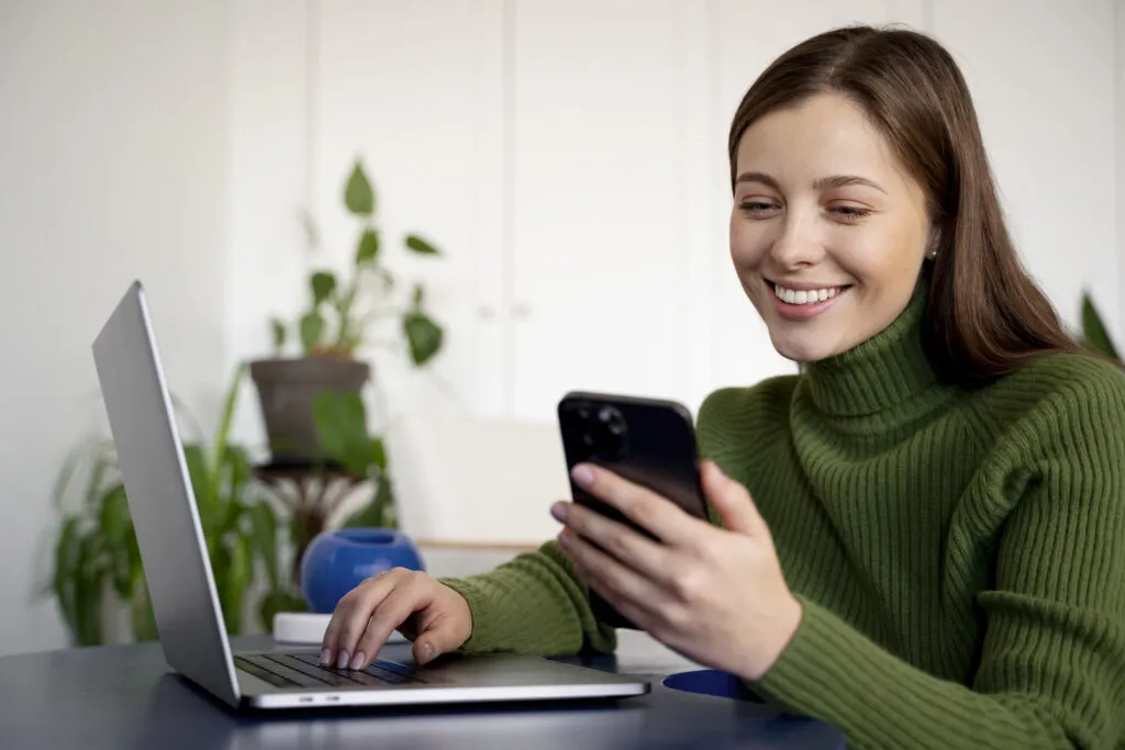 woman talking her smartphone using handsfree feature writing something her laptop