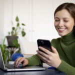 woman talking her smartphone using handsfree feature writing something her laptop