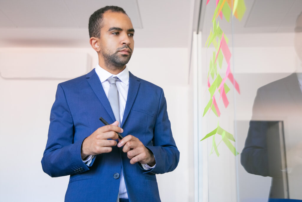 african american office employer holding pen reading notes glass wall focused confident businessman suit thinking about idea project