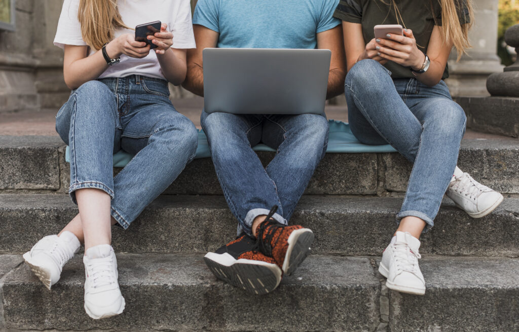 teens sitting stairs working phones laptop