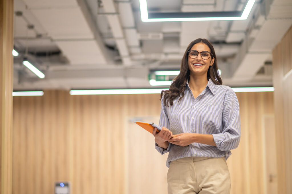 woman with folder smiling camera indoors 1 1
