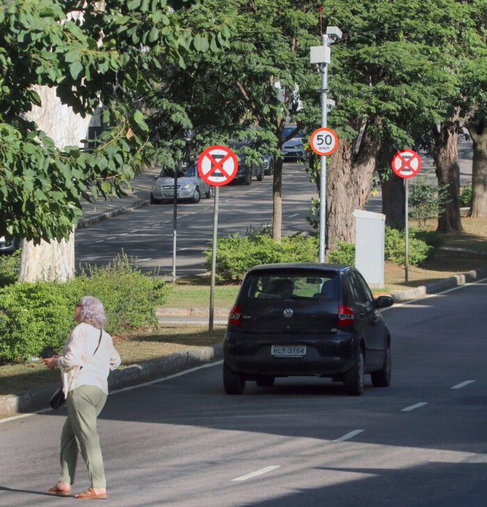 Radares aplicam mais de 75 mil multas em Juiz de Fora em seis meses 2 Mariza José Guedes de Andrade dirige o dia todo para fazer entregas. Um dos trechos que ela mais passa recebeu um novo radar: na Avenida Barão do Rio Branco 4456, Bom Pastor, para fiscalizar o excesso de velocidade no sentido Centro/Bairro, com limite de 50 km/h. Mariza acredita que a instalação foi positiva, apesar de acreditar que deveria ter sido um pouco mais para baixo na rua. "Tem um cruzamento que frequentemente é cenário de acidentes, sobretudo envolvendo motocicletas. Também há muitos idosos na área, então fica mais perigoso. Como fica mais para cima, os veículos ainda passam em alta velocidade e só reduzem perto do radar - isso quando freiam."Em situação semelhante, Roberto Barroso é motorista e dirige por toda a cidade de Juiz de Fora ao longo do dia. Durante os diferentes itinerários, independente da região, uma coisa é certa: ele irá passar por radares no trajeto. Apesar de achar a fiscalização necessária, a instalação em certos pontos gera questionamentos. "Ficamos na dúvida se a motivação foi, de fato, controlar o trânsito." Do início da cidade, no Salvaterra, até a extensão da Zona Norte (e em todas as outras regiões), Juiz de Fora tem 41 radares de trânsito em funcionamento atualmente, de acordo com a Prefeitura do município. Além disso, outros seis pontos de fiscalização estão em processo de remanejamento e ainda aguardam a aferição dos equipamentos pelo Inmetro para entrarem em operação. Ainda há 13 locais que já tiveram equipamentos instalados anteriormente. Esses pontos possuem a estrutura necessária para fiscalização, mas, no momento, estão inativos. Só no primeiro semestre de 2026, foram registradas 113.637 multas em Juiz de Fora - 75.517 delas por radares, o que representa aproximadamente 66,46% do total, ou cerca de duas a cada três. As demais são aplicadas por agentes de trânsito. Foram arrecadados R$ 14.723.262,67, enquanto R$ 17.056.847,98 dos recursos foram aplicados em sinalização, engenharia de tráfego e de campo, policiamento e fiscalização, educação de trânsito e repasse ao Fundo Nacional de Segurança e Educação de Trânsito. Os números divergem porque podem incluir despesas de exercício anterior e restos a pagar. A arrecadação e a aplicação dos recursos de multas em Juiz de Fora são divulgadas mensalmente no Portal da Transparência. Por lei, os recursos obtidos através de multas de trânsito só podem ser destinados a sinalização, engenharia de tráfego, educação para o trânsito, fiscalização e processamento de autuações. Quanto à instalação dos equipamentos, a Prefeitura diz que segue estudos técnicos da SMU e normas do Código de Trânsito Brasileiro, Conselho Nacional de Trânsito e Inmetro. Questionamentos sobre quantidade Há dois tipos de radar no município: os de velocidade e os mistos - que fiscalizam tanto a velocidade e como avanço de sinal vermelho ou parada sobre a faixa de pedestres em cruzamentos semaforizados. Em relação às localizações dos equipamentos, com as experiências já vividas no trânsito juiz-forano, Roberto questiona as instalações. "Por exemplo: tiraram equipamentos em frente ao Parque da Saudade e no Bairro Grama, que eram locais de necessidade. Por outro lado, colocaram um antes do Shopping Jardim Norte e outro na esquina da Américo Lobo com a Avenida Rio Branco - que já geram dúvidas. Tem o radar, a sinalização toda, mas se você vier no carro conversando com alguém, acaba esquecendo." Só em 2025, Roberto foi multado cerca de cinco vezes por excesso de velocidade. Mesmo com os questionamentos e as penalizações sofridas, o motorista faz questão de destacar que não é contra a medida. "A implantação de radares é fundamental, mas não há necessidade de ter tantos em Juiz de Fora - nem tem espaço para isso. Tem um próximo ao Demlurb de 40 km/h, antes da Vila Ideal. Deveria ter essa fiscalização em porta de escolas ou na Avenida Rio Branco." Durante itinerário por diferentes pontos da cidade, a Tribuna constatou que alguns radares contam com dificuldades de visualização da localização e sinalização. Enquanto uns ficam escondidos em meio a árvores e fios em postes, alguns pontos têm a sinalização horizontal de difícil percepção. Até mesmo a vertical pode ter acessibilidade dificultada: no caso de um dos equipamentos na Avenida Presidente Juscelino Kubitschek, a placa que indicava sua presença à frente estava virada, impossibilitando a leitura por parte dos motoristas. LEIA TAMBÉM: Após acidentes fatais, radar é instalado no acesso ao Viaduto Roza Cabinda e em outros 5 pontos Novos radares em Juiz de Fora A Prefeitura informou que, em 2026, não houve ampliação do número de equipamentos, mas sim a redistribuição de pontos, com base em estudos técnicos da Secretaria de Mobilidade Urbana; já em 2025, a fiscalização foi ampliada em seis pontos sensíveis. "A revisão dos locais é contínua e considera a dinâmica urbana, sendo todos os pontos, como a Rua Santo Antônio, avaliados tecnicamente para definir a medida mais adequada", afirma a PJF. Além disso, foi ressaltado que estudos conduzidos pela secretaria apontaram redução de infrações e melhora no comportamento dos motoristas nos locais anteriores, o que permitiu a transferência do monitoramento para outras vias. "A definição dos locais foi feita com base em estudos técnicos de trânsito realizados pela SMU, considerando índices de acidentes, volume de tráfego e necessidades de ordenamento viário. A medida também leva em conta demandas da população por ações voltadas à redução de velocidade e à organização do tráfego." O equipamento recentemente instalado no Bom Pastor, por exemplo, já gerou impacto. Apesar de, conforme reforça o Município, o radar não estar em funcionamento, os motoristas já desaceleram para passar por ele. Por ser um trecho de subida, a dinâmica interfere no tráfego de veículos de grande porte, como ônibus e caminhões, que precisam frear na subida - conforme presenciado pela reportagem. Entre janeiro e abril de 2026, Juiz de Fora registrou mais de 2,3 mil acidente de trânsito, segundo o Painel de Acidentes da Secretaria de Estado de Justiça e Segurança Pública (Sejusp-MG). O HPS atendeu quase 1,7 mil vítimas no mesmo período. A Tribuna questionou os locais de maior incidência de ocorrências, mas não obteve resposta. Equipamentos demandam conscientização Apesar da repercussão negativa por parte da população em instalação de radares e uma possível "indústria da multa", o engenheiro, arquiteto e professor da Universidade Federal de Juiz de Fora (UFJF) Fabio Lima reitera que os equipamentos estão entre os mecanismos e ações possíveis para manter a segurança do trânsito. "Eles inibem a velocidade pois os condutores têm a certeza de que a multa será aplicada, no caso de terem sido registrados. Se seguissem os limites e respeitassem a sinalização, os dispositivos não seriam necessários." Além disso, estão regulamentados e atrelados às políticas públicas relacionadas com a mobilidade urbana para a redução da velocidade, diminuição da imprudência e evitar a distração. "O que percebemos no cotidiano, e Juiz de Fora mostra isso, são situações de velocidades excessivas, que revelam a ansiedade e a afobação dos condutores dos veículos motorizados, sejam eles associados ao transporte público ou privado. Se os radares são vistos pela população como ligados a uma 'indústria de arrecadação', essa questão deve ser levada ao Conselho Municipal de Transportes e Trânsito (CMTT), vinculado à Secretaria de Mobilidade Urbana." O que falta na cidade, na visão de Fabio, é uma campanha de conscientização contínua para educação no trânsito - incluindo o ensino fundamental, médio e o ensino superior, além da extensão para as comunidades -, o que a coloca como um direito de todos e constitui dever prioritário da parte da Administração pública. "A velocidade dos veículos motorizados é um fator de risco para pedestres e ciclistas e para os próprios condutores desses veículos, pelos acidentes gerados, alguns com perda de vidas ou traumas físicos, com fraturas e lesões graves, e mesmo danos psicológicos", reforça. Além dos pontos de fiscalização eletrônica, outras medidas são instaladas como mecanismos para aumentar a segurança no trânsito. O professor da UFJF lembra das faixas de travessia em nível, popularmente conhecidas como lombadas. "Essas também, juntamente com as ondulações fazem com que a velocidade seja reduzida de maneira obrigatória." Rotatórias e estreitamentos de vias também inibem a velocidade. Mesmo com as possibilidades, Fabio defende que a fiscalização deve ser intensificada, pois o número de veículos motorizados aumenta a cada ano. "A sinalização vertical e horizontal implementada nas zonas diversificadas da cidade permite também a redução da velocidade, mas dependem da conscientização geral, que está relacionada às campanhas." Necessários, mas pontuais Embora ressalte a importância da presença de radares nas diferentes vias da cidade, Fabio acrescenta que a medida é pontual, já que antes e depois as velocidades máximas permitidas nos trechos seguem sendo extrapoladas. Para o professor, os dispositivos visam também amenizar as precariedades relacionadas ao sistema viário urbano para a segurança dos pedestres e ciclistas, mas as outras medidas também devem ser utilizadas para a diminuição da velocidade de maneira geral na cidade e o aumento da segurança, o que gera repercussões em todos os níveis. "A redução dos atendimentos nos hospitais e os traumas físicos e psicológicos gerados e, no extremo, não termos a perda de vidas pela velocidade, imprudência ou distração." Por fim, Fabio comenta que pela afobação e ansiedade dos condutores, ao pensar apenas no deslocamento e na chegada o mais rápido possível, sem levar em conta as consequências da imprudência, dispositivos como os radares irão aumentar, muito além dos 41 pontos de fiscalização eletrônica atuais, para a segurança de pedestres e ciclistas.